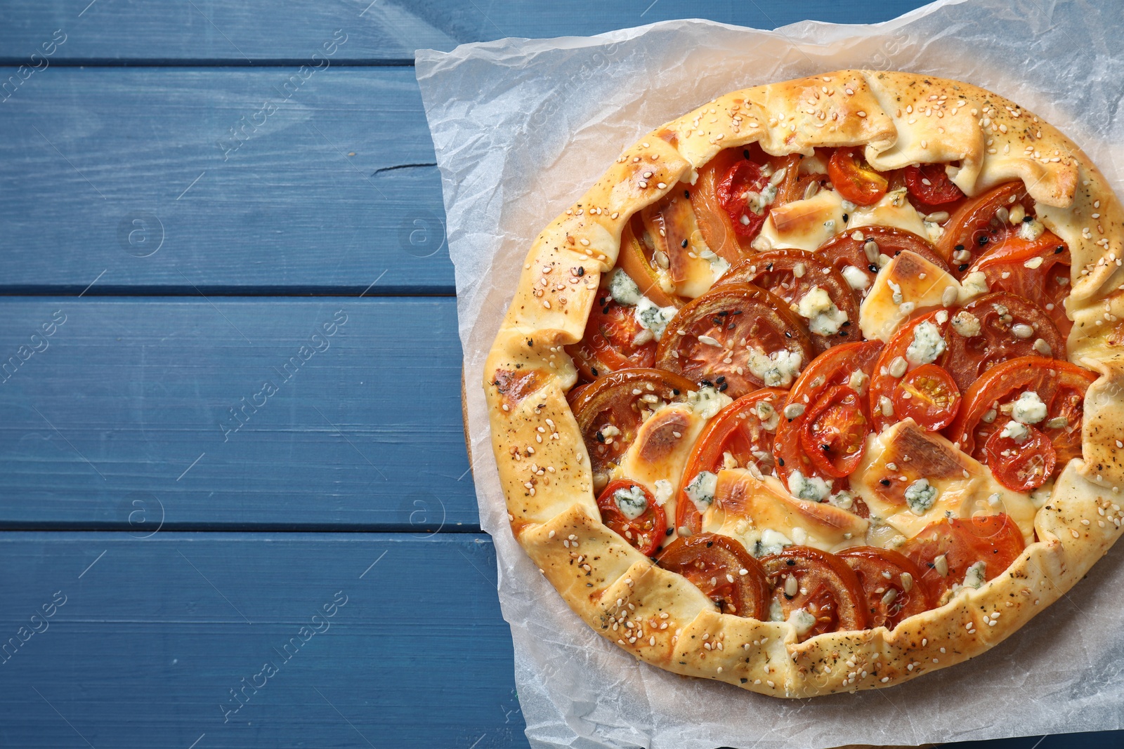 Photo of Tasty galette with tomato and cheese (Caprese galette) on blue wooden table, top view. Space for text