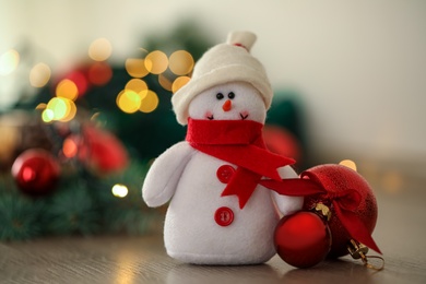 Photo of Snowman toy and Christmas balls on table against blurred festive lights, closeup