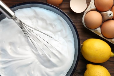 Bowl with whipped cream, whisk and ingredients on wooden table, flat lay