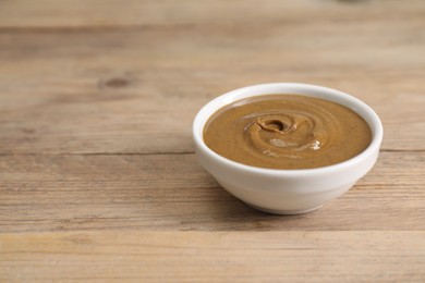 Photo of Delicious nut butter in bowl on wooden table, closeup. Space for text