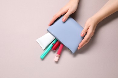 Photo of Woman with cosmetic bag and different makeup products on beige background, top view