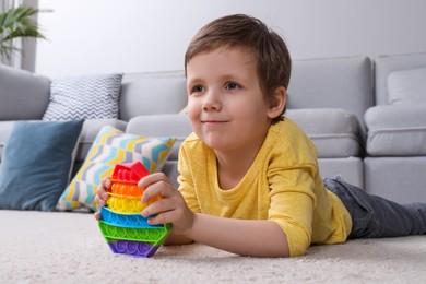 Photo of Little boy playing with pop it fidget toy on floor at home