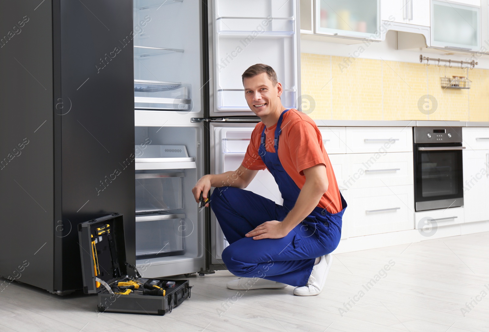 Photo of Male technician with pliers repairing refrigerator in kitchen