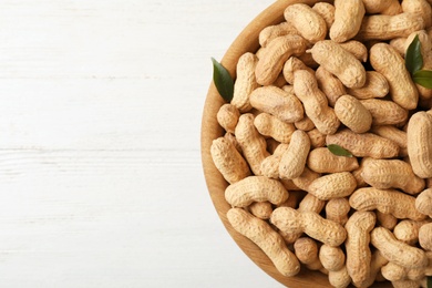 Photo of Bowl with peanuts in shell and space for text on wooden table, top view