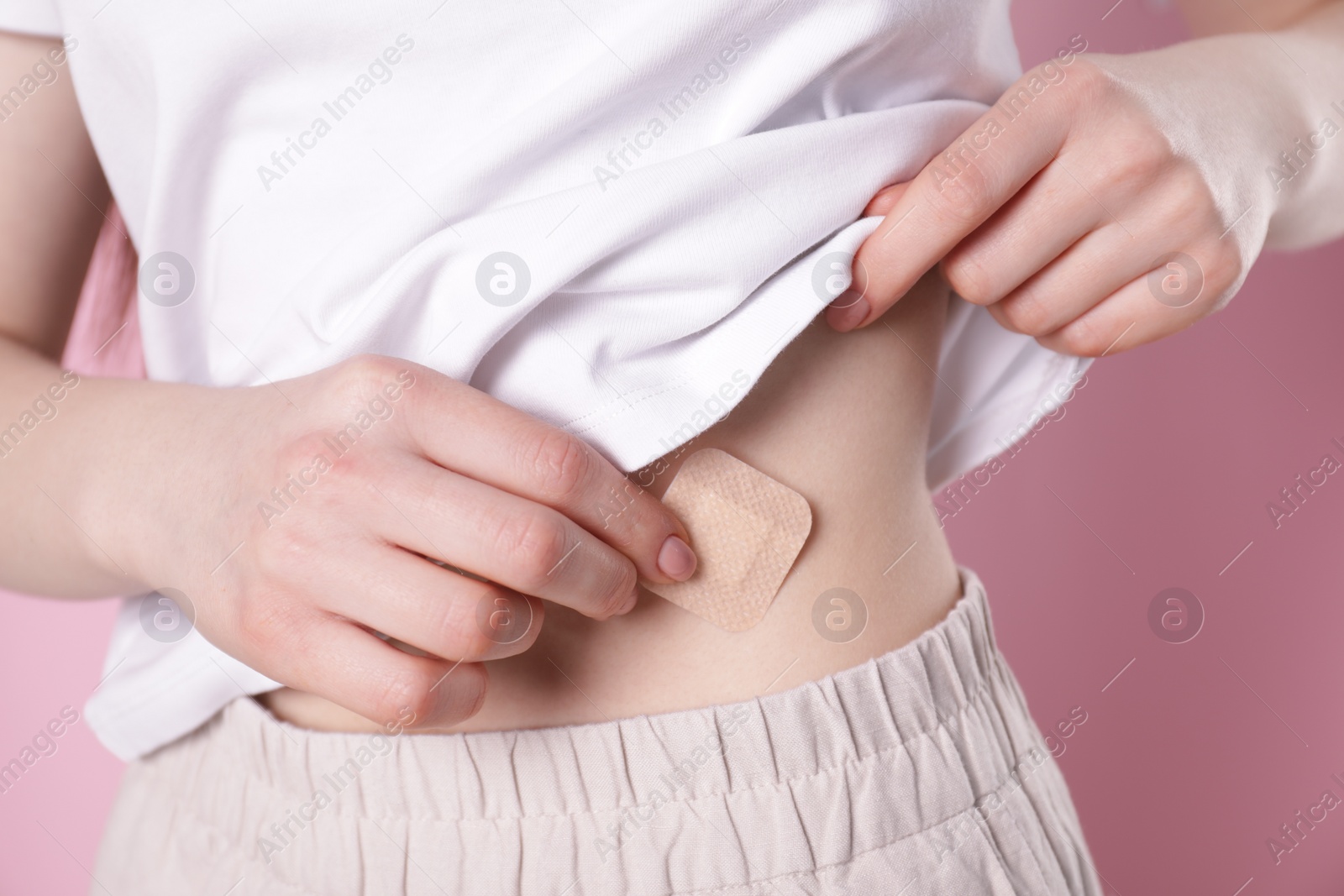 Photo of Woman applying contraceptive patch onto her body on pink background, closeup