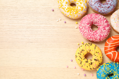 Photo of Delicious glazed donuts on wooden table, flat lay. Space for text