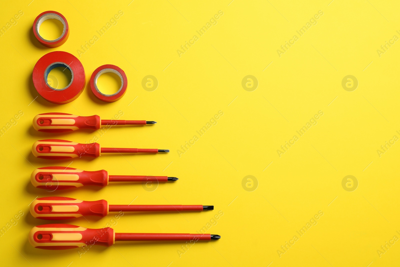 Photo of Flat lay composition with electrician's screwdrivers and adhesive tapes on yellow background, space for text