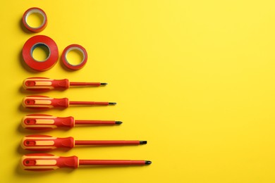 Flat lay composition with electrician's screwdrivers and adhesive tapes on yellow background, space for text