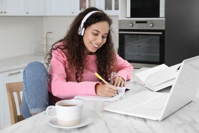 African American woman with modern laptop and headphones studying in kitchen. Distance learning