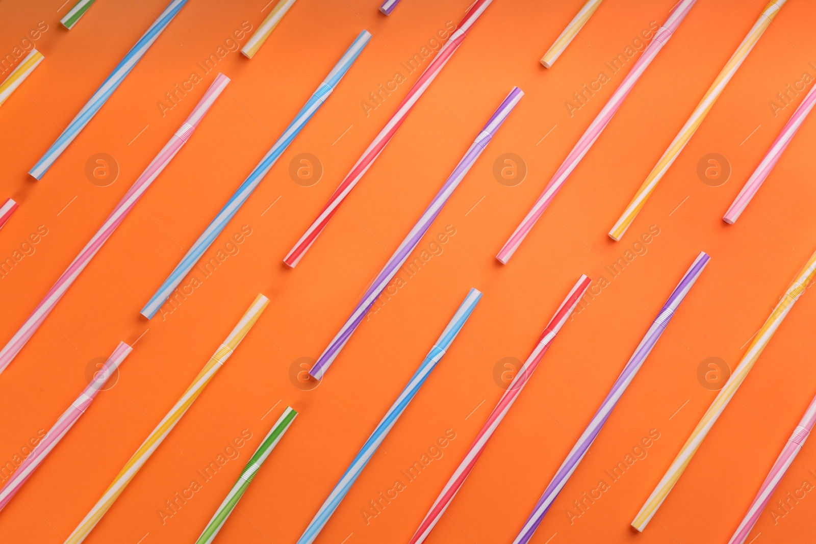 Photo of Colorful plastic straws for drinks on orange background, flat lay