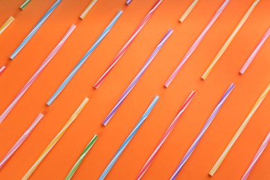 Colorful plastic straws for drinks on orange background, flat lay