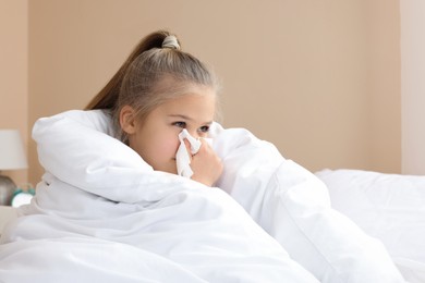 Sick girl with tissue blowing her nose in bed indoors, space for text. Cold symptoms