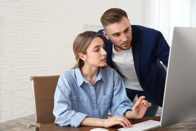 Man helping his colleague work with computer in office