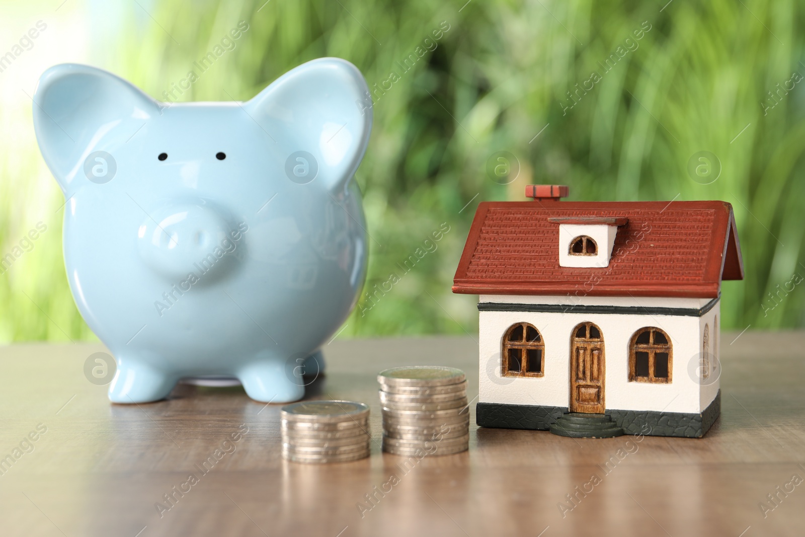 Photo of House model, stacked coins and piggy bank on wooden table outdoors