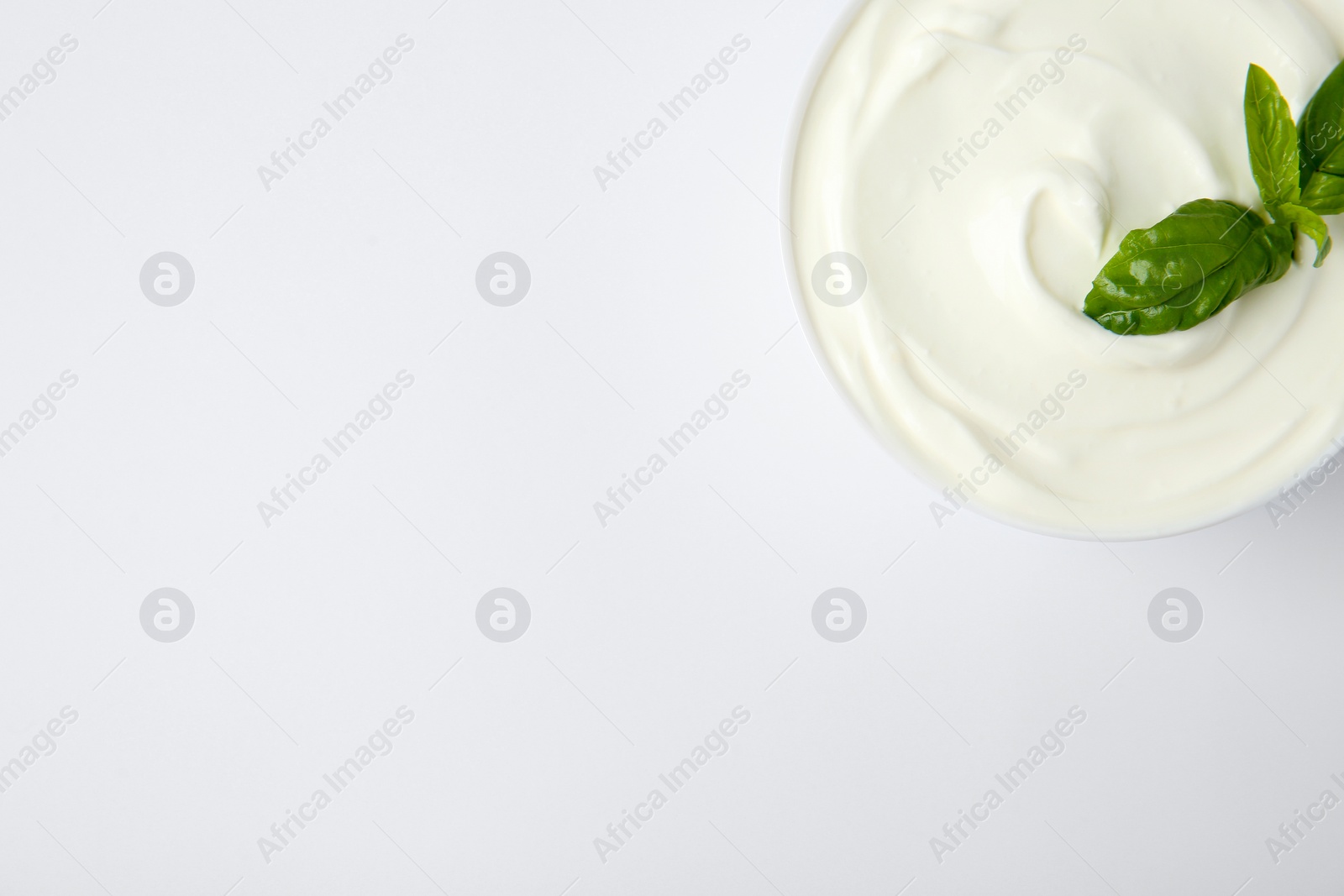 Photo of Bowl of fresh sour cream with basil on white background, top view