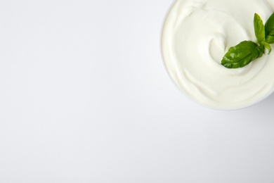 Bowl of fresh sour cream with basil on white background, top view