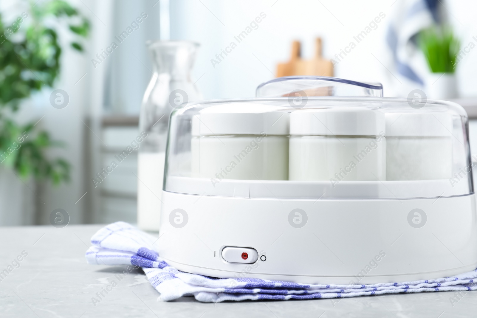 Photo of Modern yogurt maker with full jars on light grey marble table in kitchen