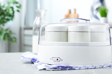 Modern yogurt maker with full jars on light grey marble table in kitchen