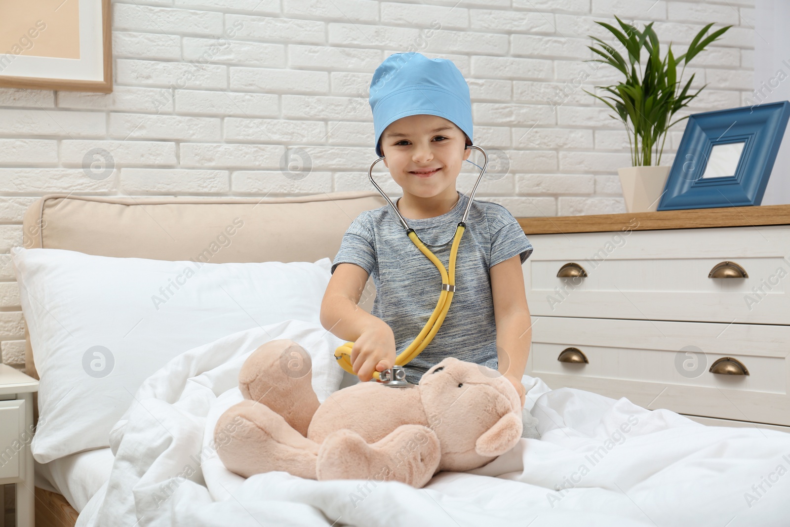 Photo of Cute child playing doctor with stuffed toy on bed in hospital ward