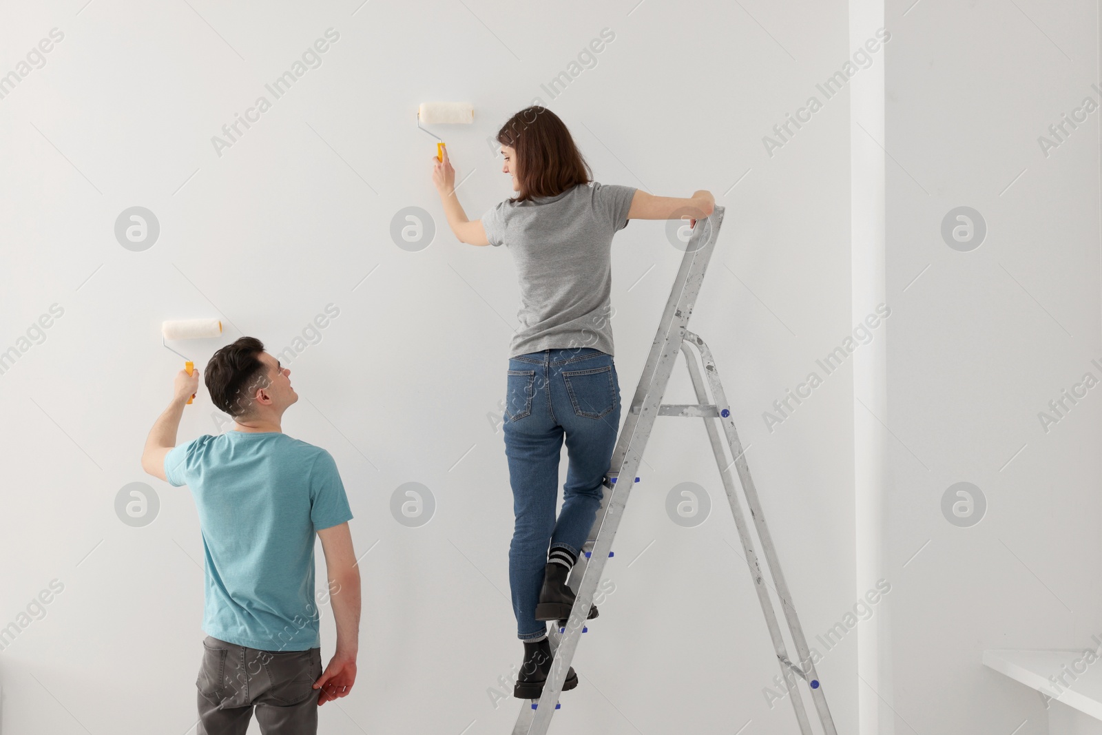 Photo of Young man and woman painting wall with rollers indoors. Room renovation