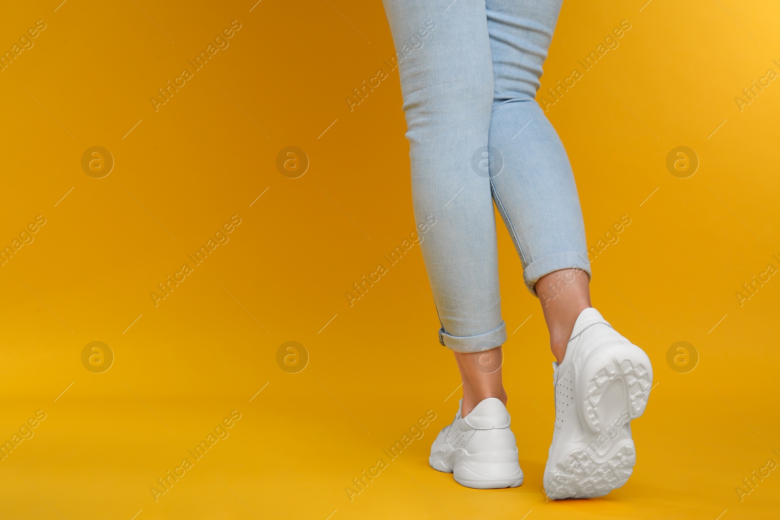 Photo of Woman wearing stylish sneakers on yellow background, closeup. Space for text