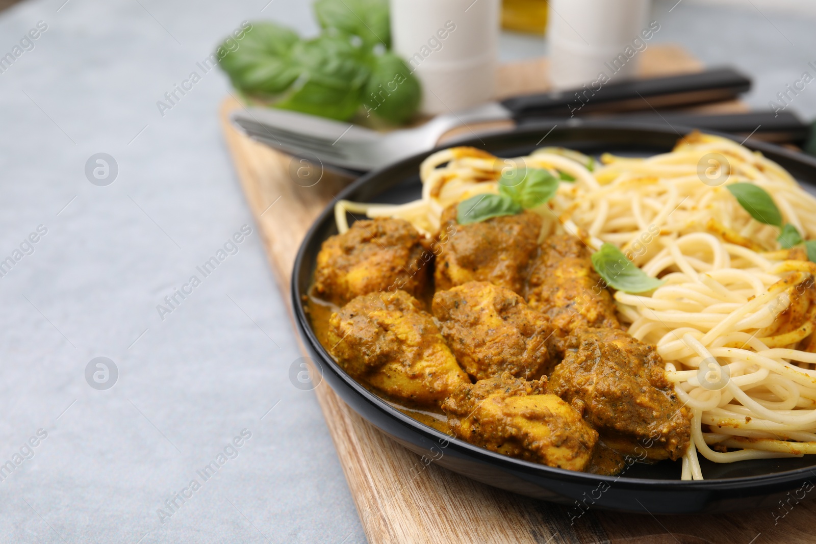 Photo of Delicious pasta and chicken with curry sauce served on grey table, closeup. Space for text