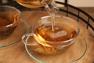 Photo of Pouring tasty tea into glass cup at wooden table, closeup