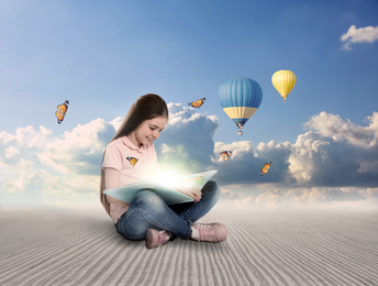 Image of Cute little girl reading magic book. Picturesque view of blue sky and air ballons on background 