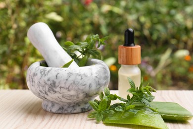 Mortar with pestle, herbs and bottle of essential oil on wooden table outdoors