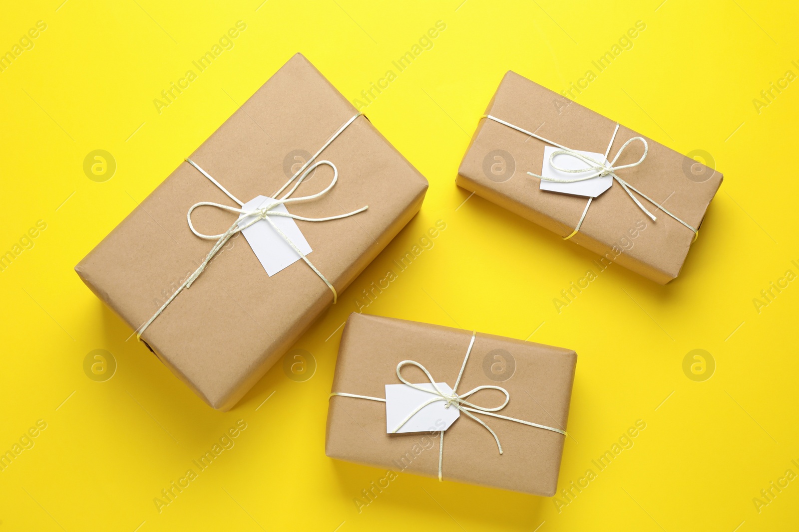 Photo of Parcels wrapped in kraft paper with tags on yellow background, flat lay