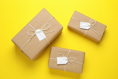 Photo of Parcels wrapped in kraft paper with tags on yellow background, flat lay