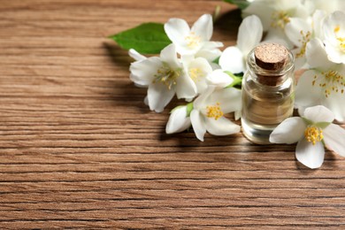 Photo of Jasmine essential oil and fresh flowers on wooden table, space for text