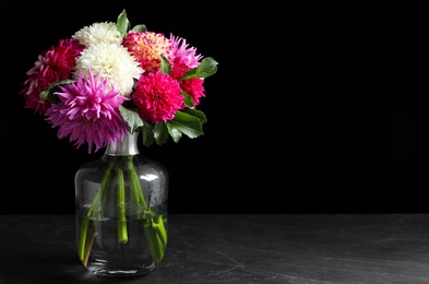 Photo of Beautiful dahlia flowers in vase on table against black background. Space for text