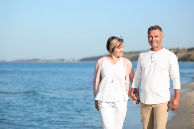 Happy mature couple walking at beach on sunny day