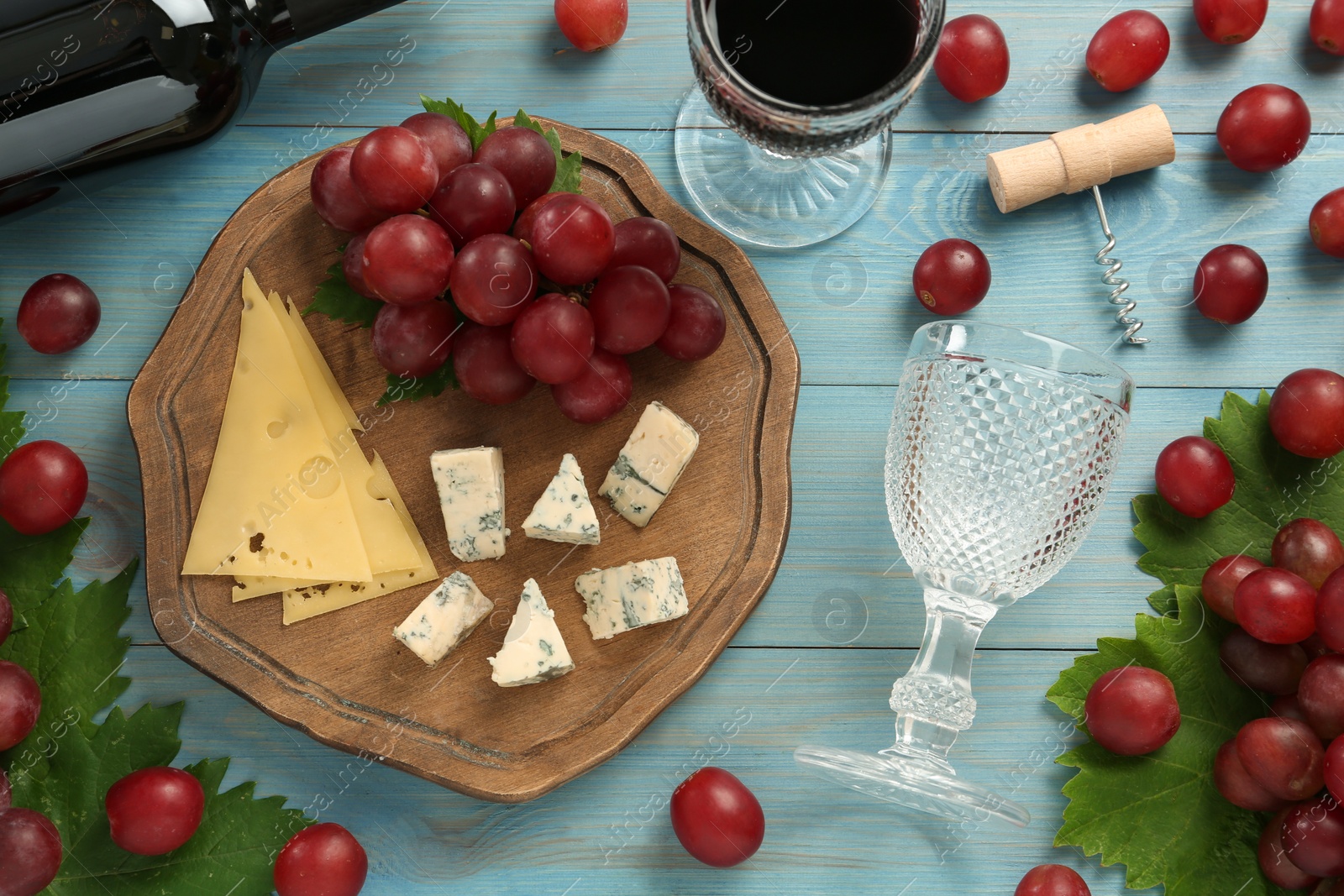 Photo of Tasty red wine and snacks on light blue wooden table, flat lay