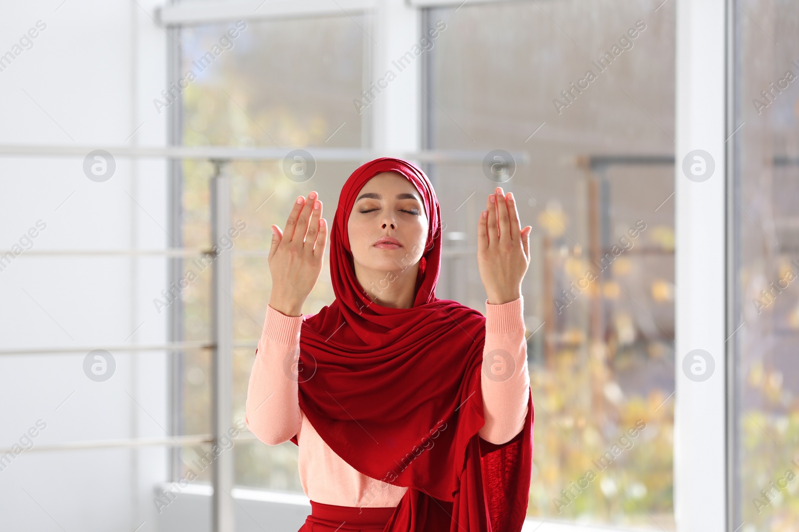 Photo of Young Muslim woman in hijab praying indoors