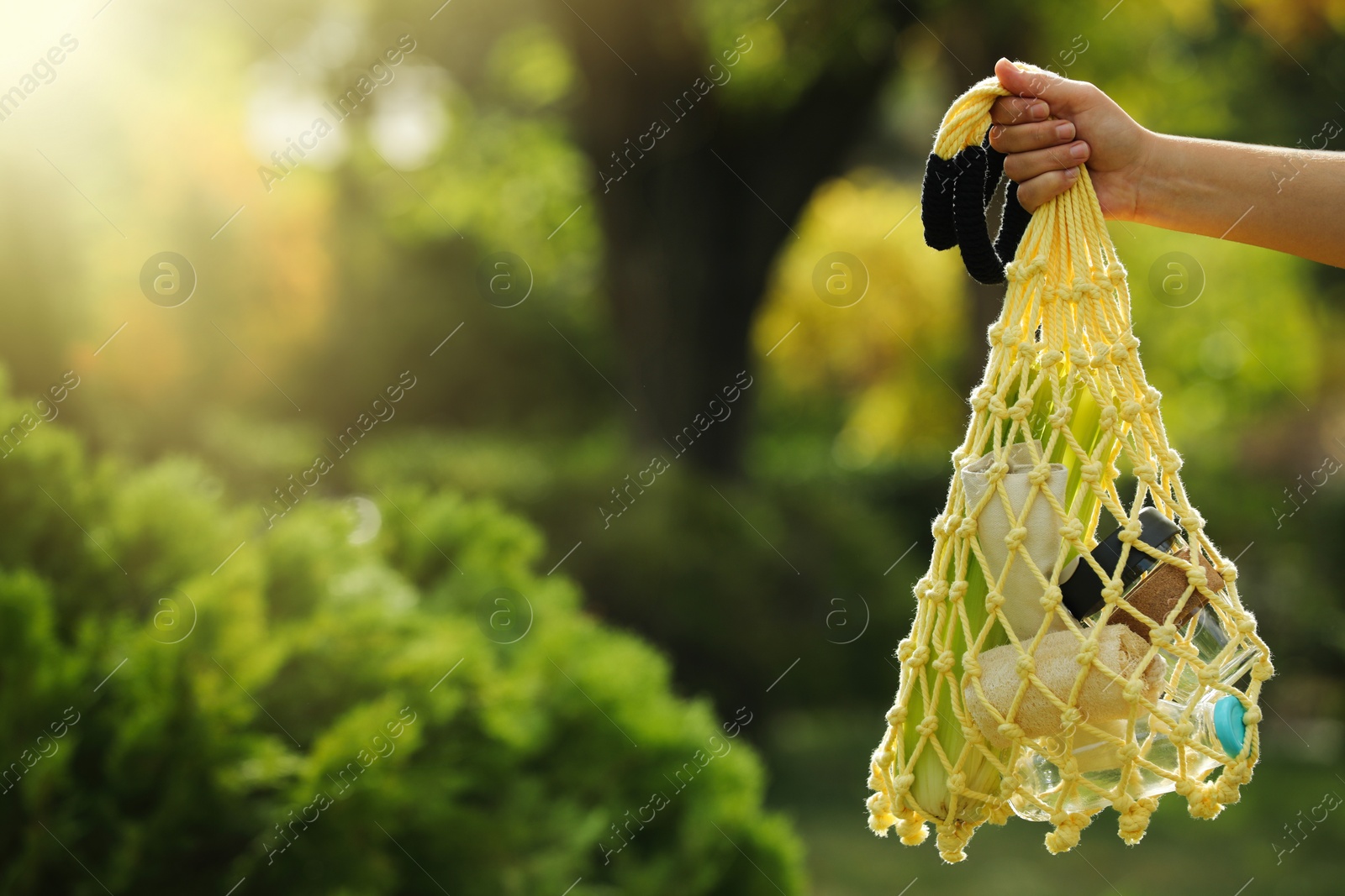Photo of Conscious consumption. Woman with net bag of eco friendly products in park, closeup. Space for text