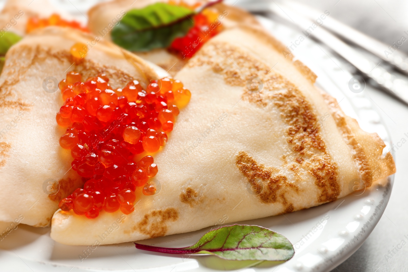 Photo of Thin pancakes served with red caviar on plate, closeup