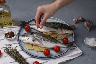 Woman salting raw dorado fish at grey table, closeup