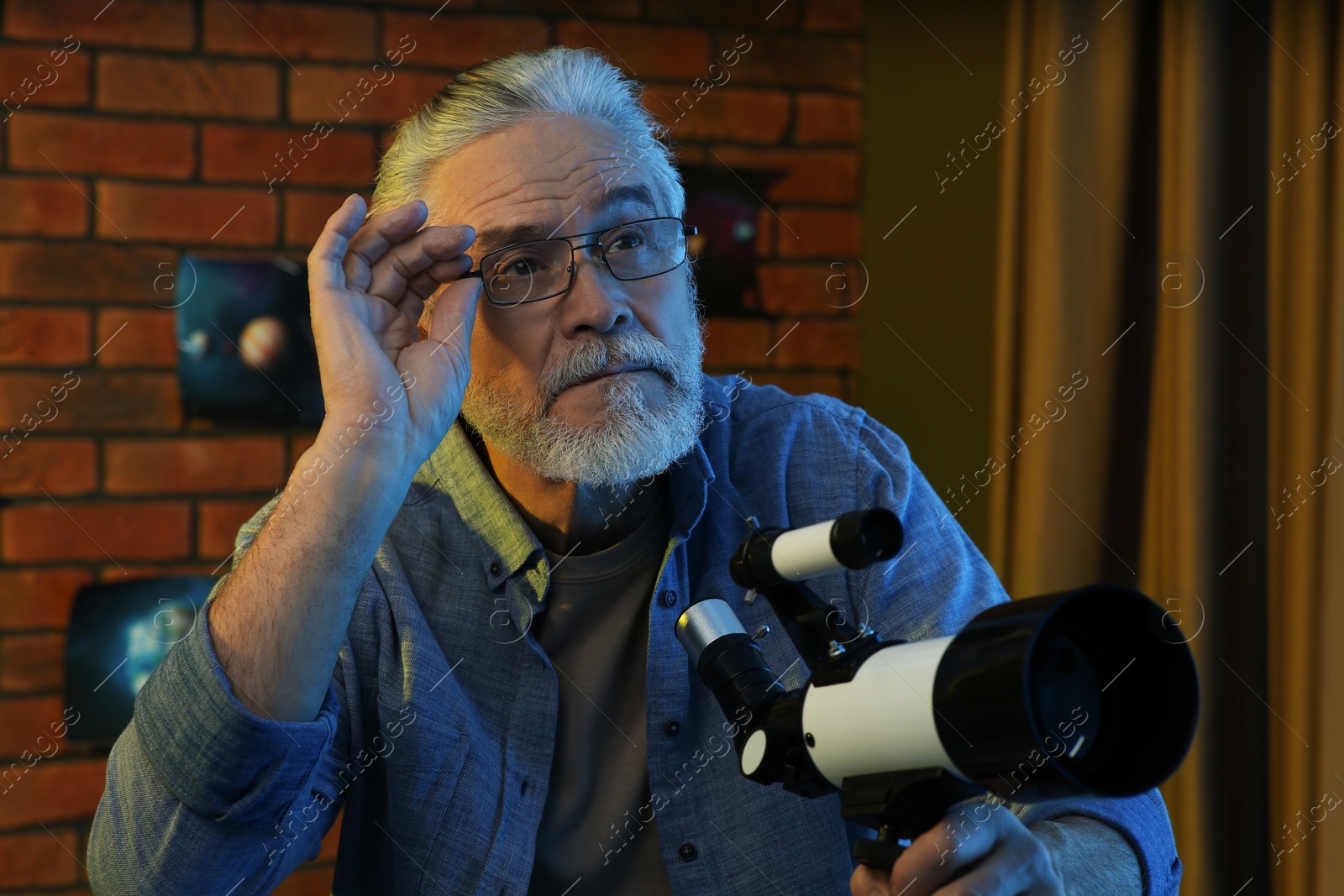 Photo of Senior man using telescope to look at stars in room