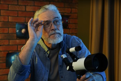 Photo of Senior man using telescope to look at stars in room