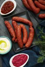 Photo of Tasty sausages and different sauces on black table, flat lay. Meat product
