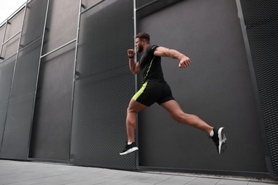 Man running near building outdoors, low angle view. Space for text