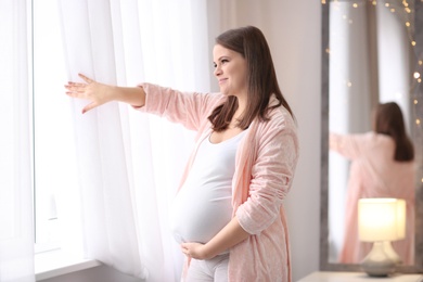 Beautiful pregnant woman standing near window at home