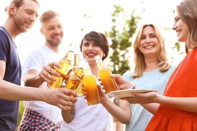 Photo of Young people with bottles of beer and food outdoors. Summer barbecue