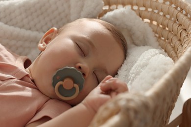 Photo of Cute little baby with pacifier sleeping in wicker crib, closeup