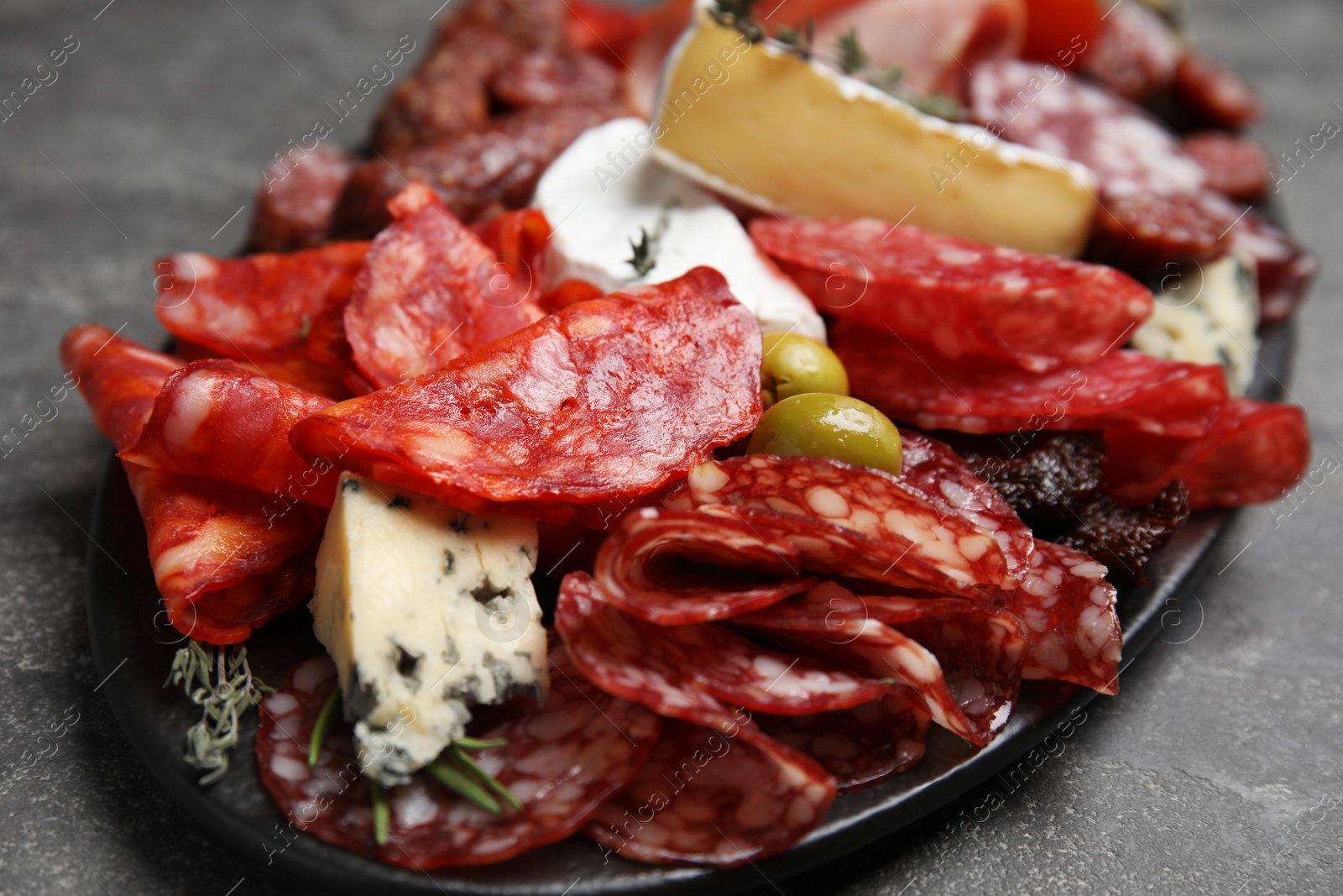 Photo of Tasty salami and other delicacies served on grey table, closeup