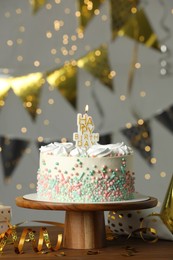 Beautiful birthday cake with burning candle and decor on wooden table