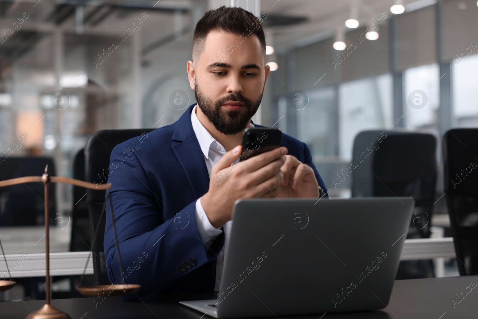 Photo of Serious lawyer with smartphone near laptop at table in office