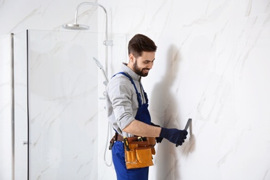 Photo of Handyman working with putty knife in bathroom. Professional construction tools